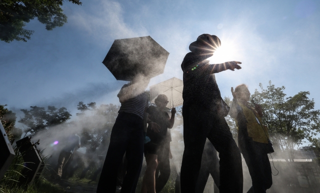 Pedestrians walk through a cooling mist with parasols in Daegu, North Gyeongsang Province on June 18, where the daytime high reached 35 degrees Celsius that day. (Yonhap)