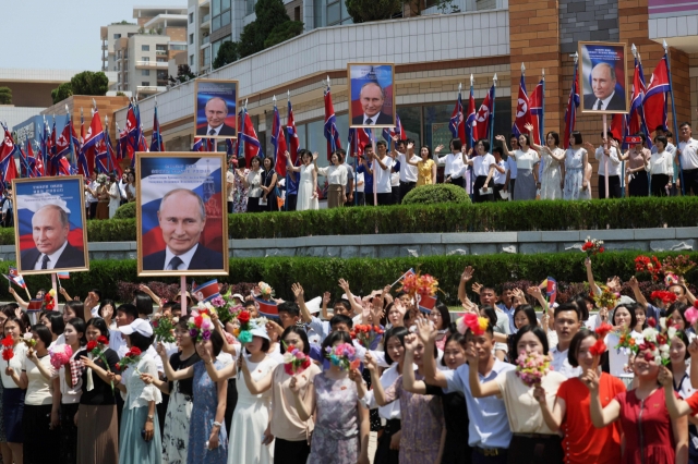 In this pool photograph distributed by the Russian state agency Sputnik, people wave to the motorcade carrying North Korea's leader Kim Jong-un and Russian President Vladimir Putin during a welcoming ceremony at Kim Il Sung Square in Pyongyang on June 19. (Pool Photo via AFP)