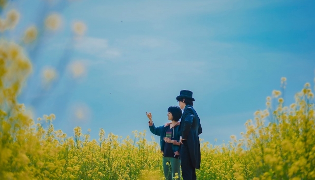 A still image shows Ah-yi and magician Ri-eul standing in a canola flower field in 