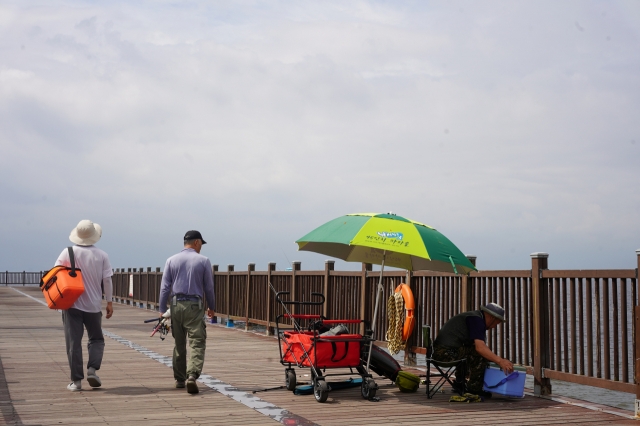 An angler prepares to fish from the wooden dock extending out over the sea on Tuesday. (Lee Si-jin/The Korea Herald)