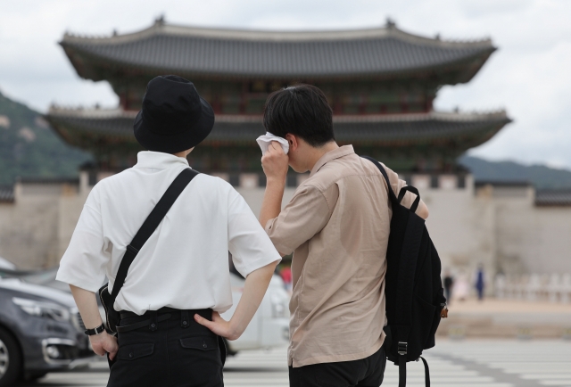 A person wipes away sweat as two people wait to cross a crosswalk near Gwanghwamun Square in central Seoul, Thursday, where daytime temperatures reached 33 degrees Celsius. (Yonhap)