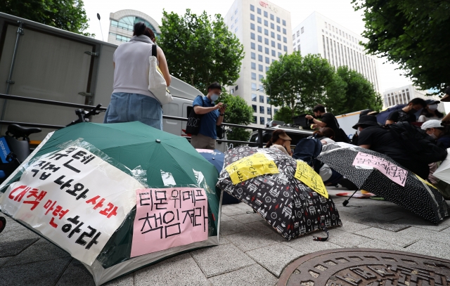 Consumers suffering from delayed payments from e-commerce platforms Tmon and WeMakePrice stage an umbrella protest, calling for apology and measures to recover damage, in front of the two platforms' owner Qoo10 headquarters in Seoul on Sunday. (Yonhap)