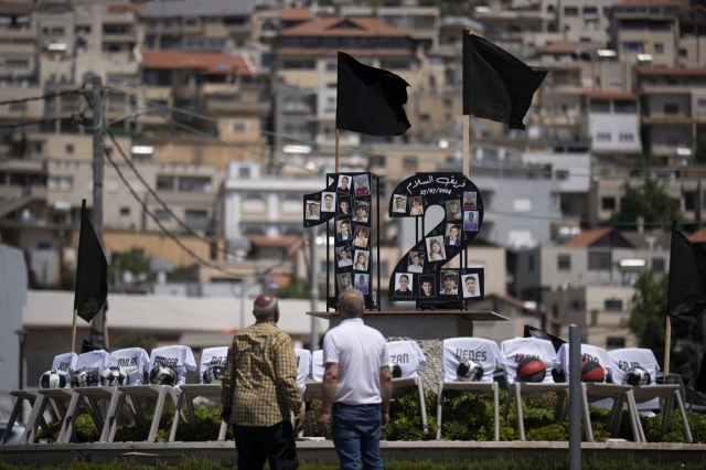 People stand in front photos of the 12 children and teens, killed in a rocket strike at a soccer field, and chairs with their names written on it, displayed on a roundabout in the village of Majdal Shams, in the Israeli-annexed Golan Heights, Tuesday. (AP-Yonhap)