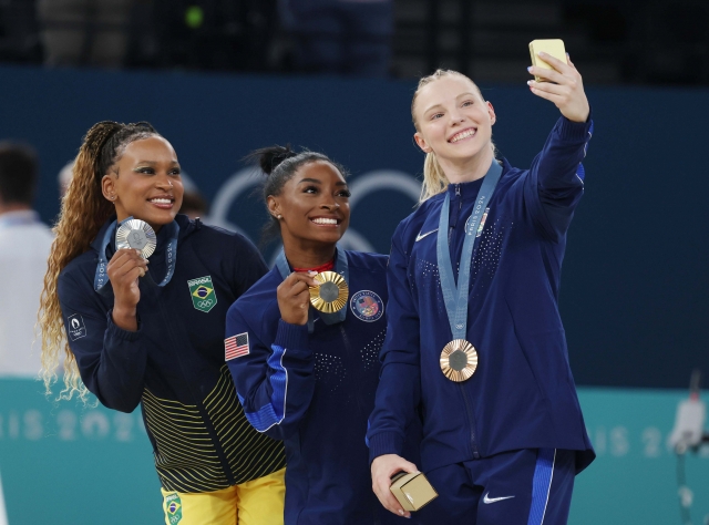 From left: Silver medalist Rebeca Andrade of Brazil, gold medalist Simone Biles of the US, and bronze medalist Jade Carey of the US take a selfie with a Samsung Galaxy Z Flip6 Olympic Edition phone during the victory ceremony of the women's vault of artistic gymnastics at the Paris 2024 Olympic Games in Paris on Saturday. (Joint Press Corps)