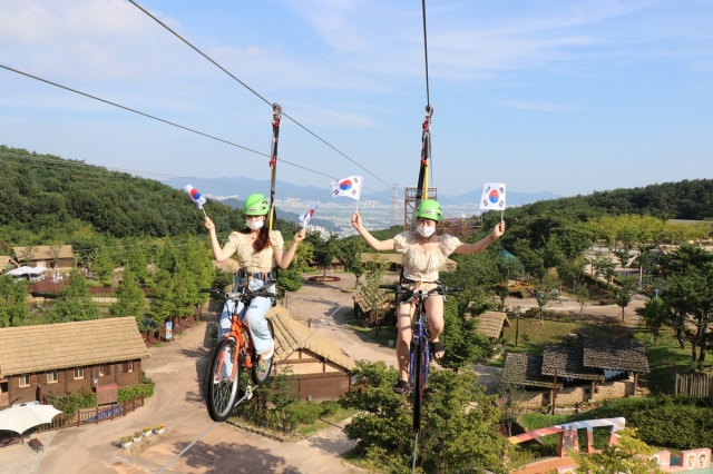 Travelers pose for photos with mini Taegeukgi while riding Exciting Cycle at Gimhae Gaya History Park in Gimhae, South Gyeongsang Province. (Gimhae City)