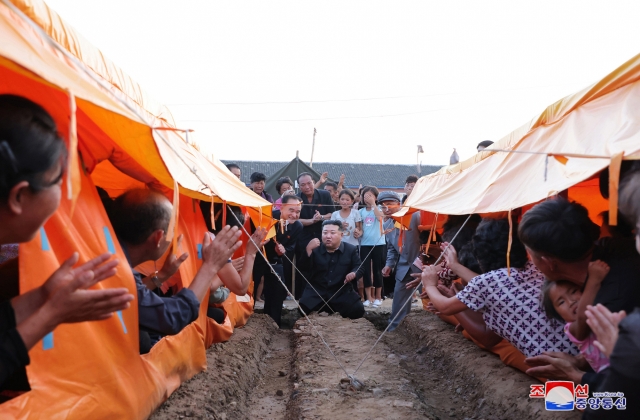 This photo, carried on Saturday, shows the North's leader Kim Jong-un (center) meeting with victims of the recent heavy rains in Uiju County in the northwestern province of North Pyongan. (KCNA)