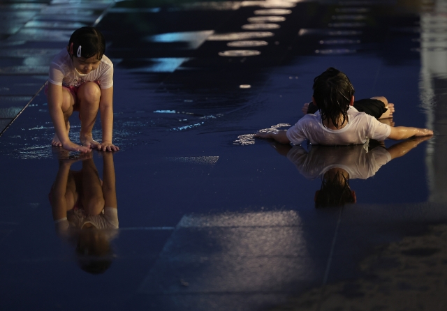 Two children cool off at a fountain in Gwanghwamun Square in central Seoul on Tuesday evening. As of Wednesday, Seoul has seen tropical nights for 24 consecutive days. (Yonhap)