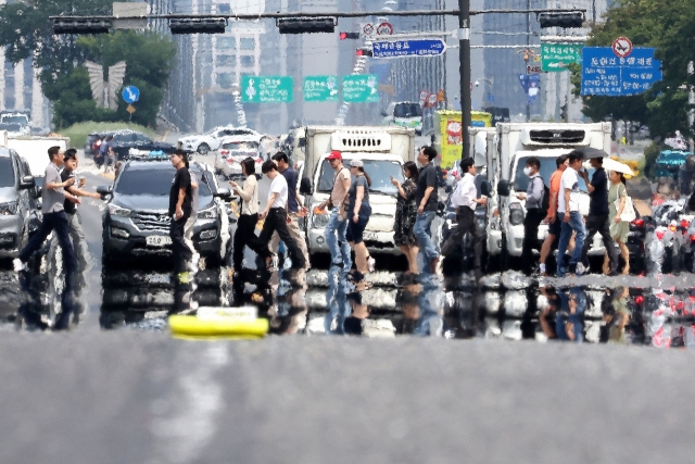 Pedestrians cross a street in Seoul on Monday amid sweltering heat. (Yonhap)