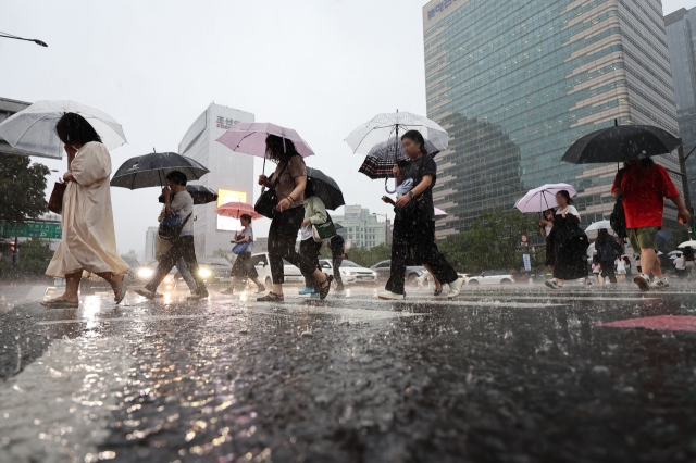 Pedestrians cross the street near Gwanghwamun Square, as a heavy rain warning was issued across the city Wednesday morning. (Yonhap)