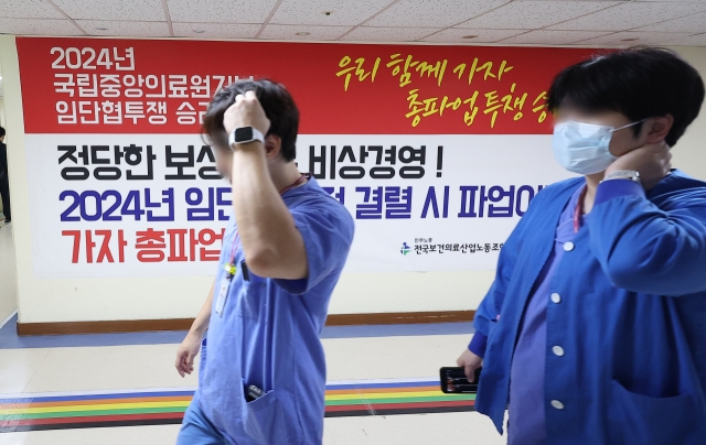 Medical workers pass by a poster posted at the National Medical Center that informs about unionized hospital workers' strike (Yonhap)