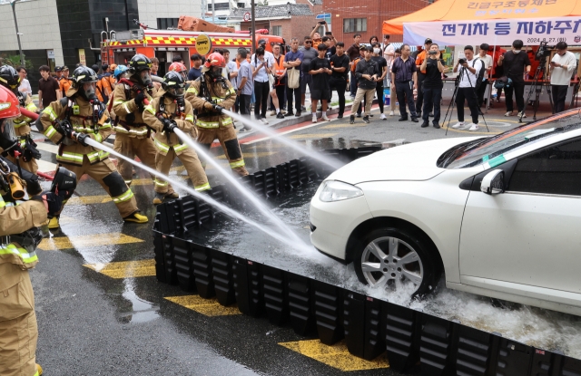 Firefighters train on how to deal with an electric vehicle fire in an underground parking lot, using a mobile immersion tank to extinguish the flames while towing the vehicle to ground level in Busan on Aug. 27. (Yonhap)