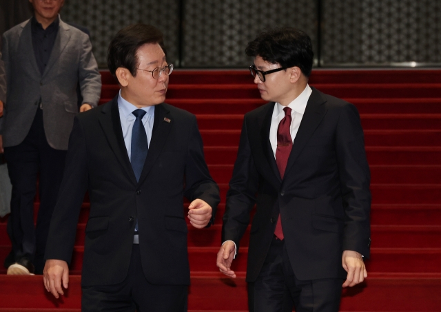 Rep. Lee Jae-myung, the Democratic Party of Korea chair, (left) and Han Dong-hoon, the People Power Party chair, speak to one another as they walk down the stairs of the National Assembly main building on Sunday. (Yonhap)