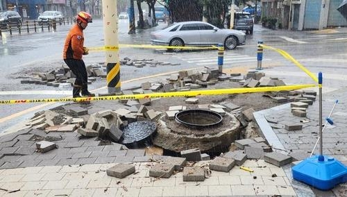 In Busan, where over 200 millimeters of rain fell, a sinkhole extends to a depth of about 8 meters, causing two vehicles to fall in, Saturday. (Yonhap)