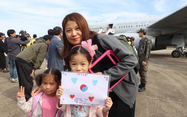 After disembarking from a military transport aircraft at Seoul Air Base on Saturday afternoon, following their departure from Lebanon on Friday, children hold up a sign featuring the South Korean national flag design that reads: 