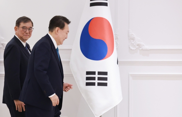 President Yoon Suk Yeol (right) and Japanese Prime Minister Shigeru Ishiba walk past South Korea's national flag as they met at a hotel in Vientiane, Laos, on Thursday. (Yonhap)