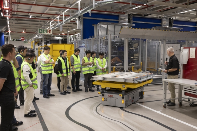 Korean reporters observe an automated guided vehicle transporting battery modules along the factory floor. (Mercedes-Benz)