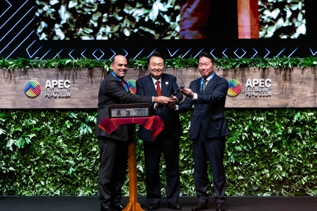 President Yoon Suk Yeol (center) and Chey Tae-won (right), chairman of the Korea Chamber of Commerce and Industry, who will serve as the chair of the 2025 APEC CEO Summit, receive the gavel from Fernando Zavala (left), chair of the 2024 APEC CEO Summit held at the Grand National Theater in Lima, Peru, on Friday (local time). (Yonhap)