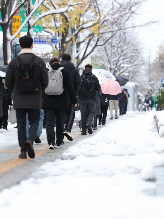 People navigate snow-covered roads near Gwanghwamun Square, central Seoul, on Thursday (Yonhap)