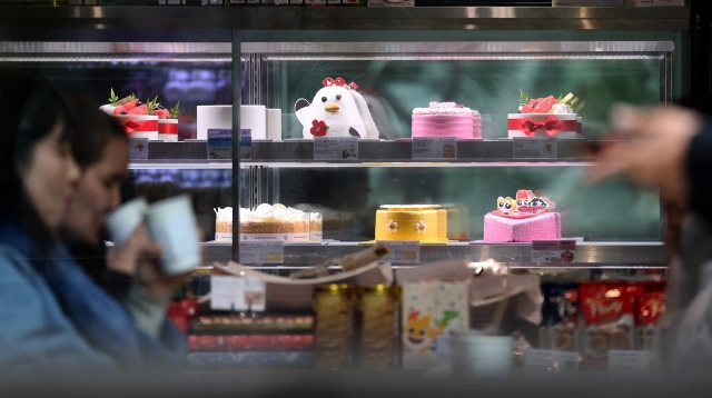 Customers enjoy drinks near a display of festive Christmas cakes at a local bakery in Seoul. (Newsis)