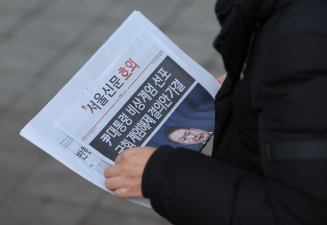 A passerby reads a special edition of a newspaper covering President Yoon Suk Yeol's public address and announcement lifting martial law near Jonggak Station in central Seoul on Wednesday morning. (Yonhap)