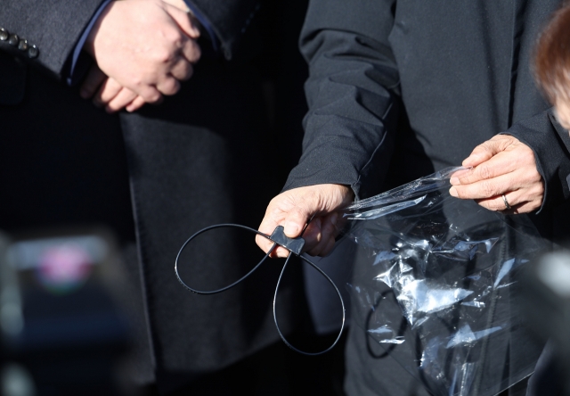 Democratic Party leader Rep. Lee Jae-myung and the party’s Supreme Council member Rep. Kim Min-seok show cable ties left behind by martial law troops during a rally held outside the National Assembly building in Yeouido, Seoul, Wednesday. (Yonhap)