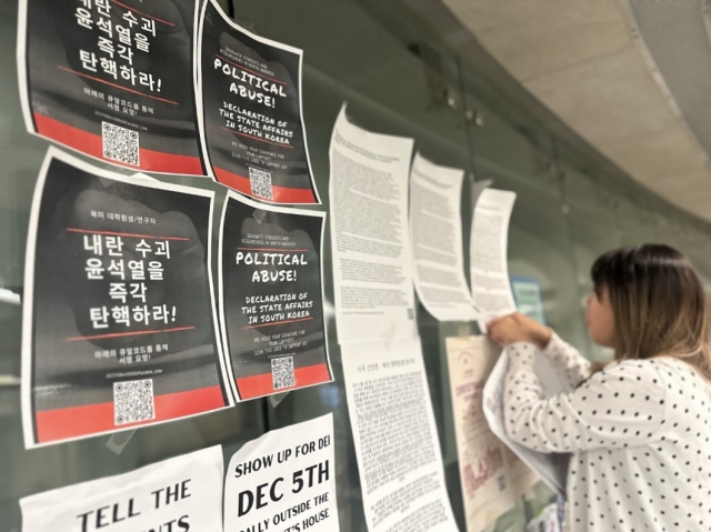 A woman posts anti-Yoon Suk Yeol posters on Thursday as North American scholars join in criticism. (Graduate Students and Researchers Across North America)