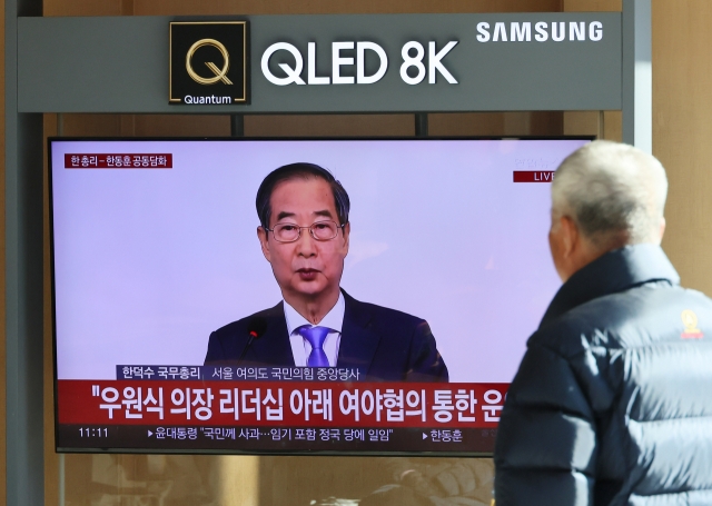 A passerby watches Prime Minister Han Duck-soo deliver a joint public address by television at Seoul Station, Sunday. (Yonhap)