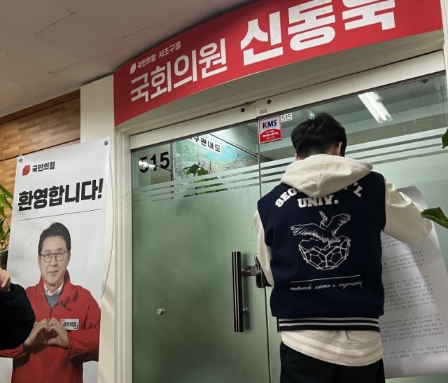 A Seoul National University student displays a poster on the front door of Rep. Shin Dong-uk’s local office in Seocho-gu, Seoul, Monday. (Yonhap)