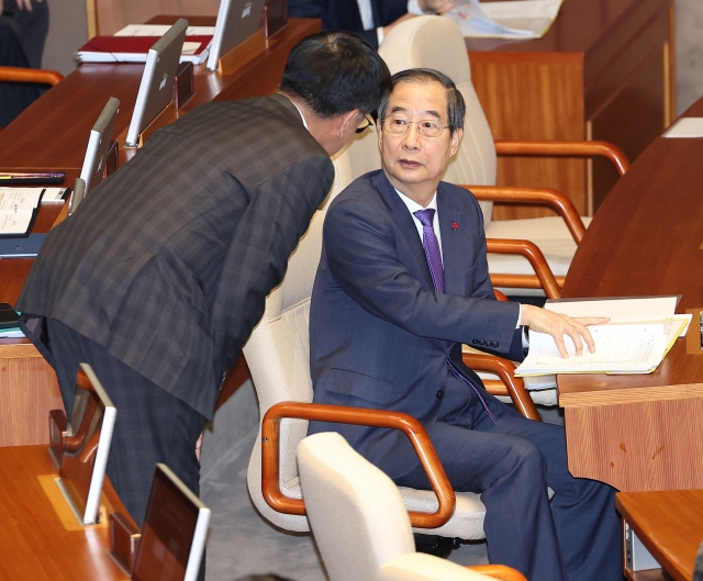 Prime Minister Han Duck-soo (right) is seen talking with Deputy Prime Minister Choi Sang-mok in the main chamber of the National Assembly on Friday. (Yonhap)