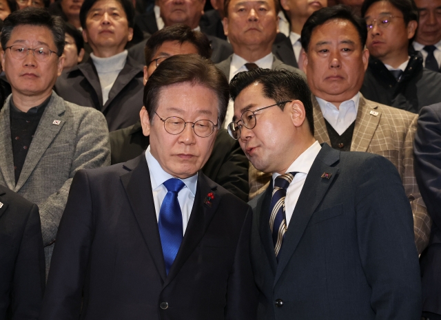 Democratic Party of Korea leader Lee Jae-myung (left) listens to floor leader Park Chan-dae as the party's lawmakers gather in front of the National Assembly's main building in Seoul after the impeachment motion against President Yoon Suk Yeol was passed on Saturday. (Yonhap)