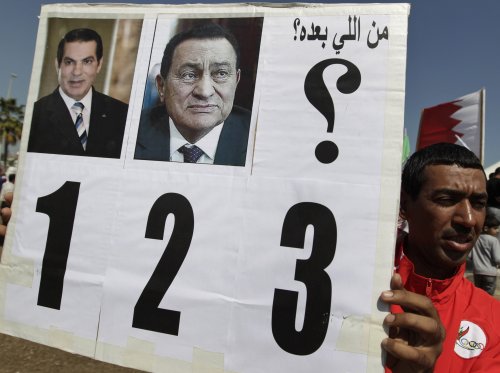 A Bahraini anti-government protester holds up a banner with pictures of former Tunisian president Zine El Abidine Ben Ali (left) and former Egyptian president Hosni Mubarak (center) and which says in Arabic “who is next?” at the Pearl roundabout in Manama, Bahrain, Sunday. (AP-Yonhap News)