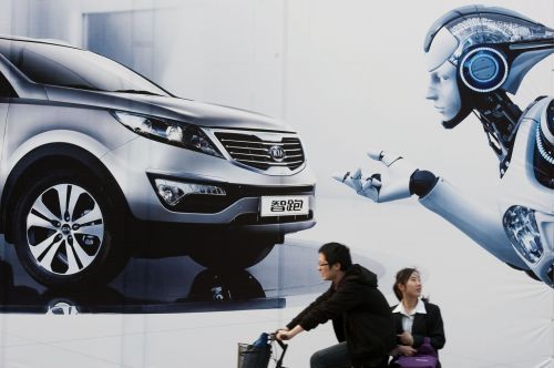 A couple cycles past a billboard outside the venue of the Auto Shanghai show in Shanghai on Thursday. (AFP-Yonhap News)