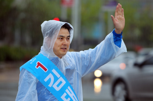 Kim Tae-ho, the ruling Grand National Party candidate for a legislative seat in Gimhae, waves to voters while campaigning in Friday’s rain. (Yonhap News)