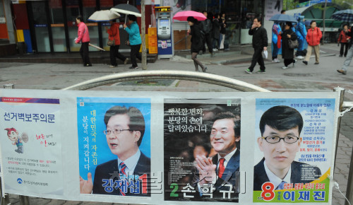 People in the Bundang-B constituency walk past the by-election posters Tuesday, the last day of the electoral campaigns. (Park Hyun-koo/The Korea Herald)