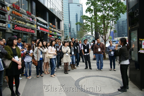 Foreign publicity ambassadors listen to a guide explaining the “media pole,” a public media art installation that functions as an information board as well as streetlight in Gangnam-daero, southern Seoul, Saturday. (Gangnam-gu Office)