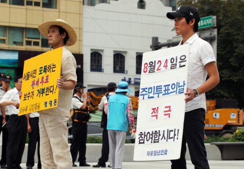 With just two days left to the referendum on free school lunches, two citizens hold pickets ― one (left) calling for a boycott of the vote and the other urging residents to cast ballots, at Gwanghwamun Square in downtown Seoul on Monday. (Yonhap News)