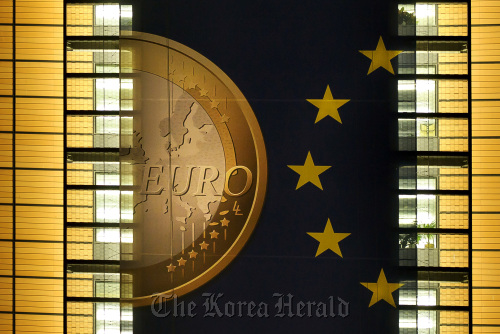 A giant euro banner, featuring an image of a euro coin and promoting stronger European economic governance, is illuminated at night as it hangs on the side of the headquarters of the European Union commission at the Berlaymont Building, in Brussels. (Bloomberg)