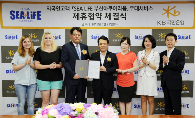 UPGRADED SERVICE FOR FOREIGNERS -- KB Kookmin Bank signs a partnership agreement with Sea Life Busan Aquarium on Tuesday, in a joint goal to offer customized service to foreign nationals. Participants included Oh Pyung-seob (fourth from left), head of customer service group at KB Kookmin Bank, and Sea Life sales and marketing director Yun Jun-young (third from left). KB Kookmin Bank