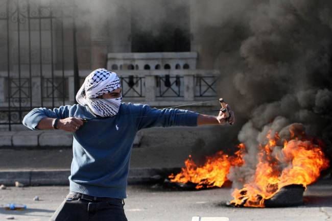 A Palestinian protester uses a slingshot to throw stones during clashes with Israeli security forces at the main entrance of the West Bank city of Bethlehem on Friday. New violence erupted in the West Bank the day before with four Palestinian attackers shot dead by Israeli forces, as Israel recoiled over a video showing Jewish extremists celebrating a Palestinian toddler`s death. (AFP-Yonhap)