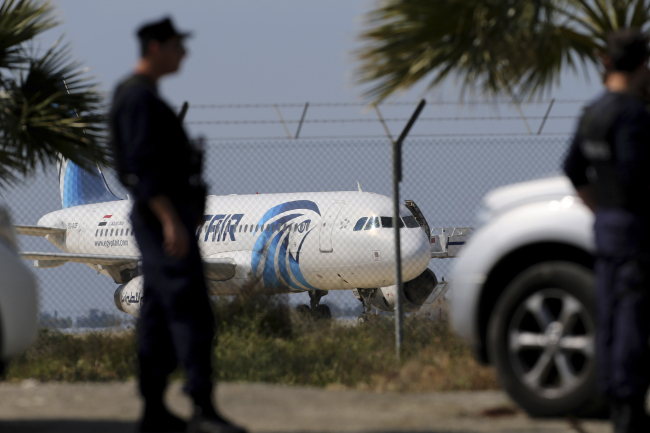 Police officers stand guards by the fence of the airport as a hijacked EgyptAir aircraft is seen after landing at Larnaca Airport in Cyprus Tuesday, March 29, 2016. (AP-Yonhap)