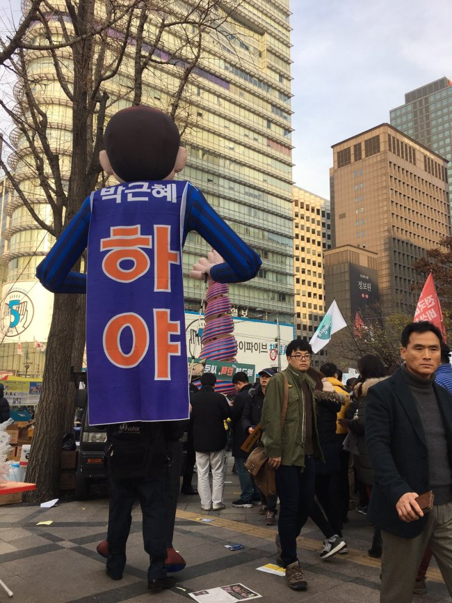 A protester in an oversize costume bears a banner on his back that reads 