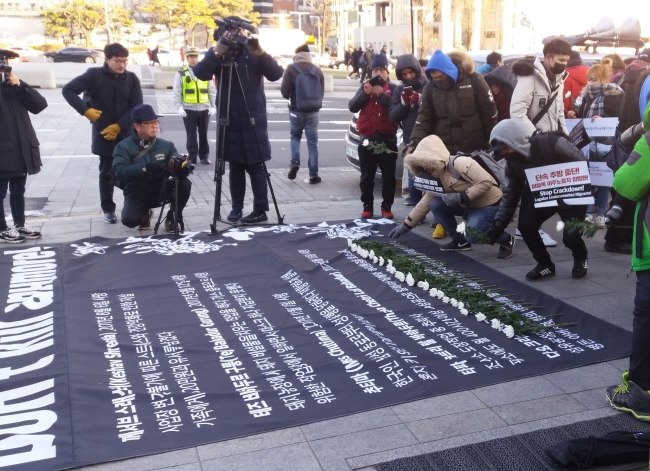 Attendees at the International Migrants Day event in central Seoul lay chrysanthemums on a banner listing the recent deaths of five foreign residents, in Seoul on Sunday. (Paul Kerry/The Korea Herald)