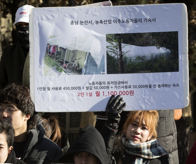 A woman holds up a poster describing living conditions of two migrant workers at the International Migrants Day event in central Seoul. (Yonhap)