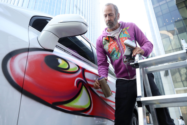 Artist Kenny Scharf spray-paints a car in front of the Lotte World Tower. The performance was part of his “Karbombz” series. (Yonhap)