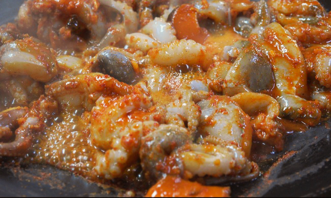 Jjukkumi, heavily doused with gochujang, is stir-fried in a large, shallow pan. (Lee So-jung/The Korea Herald)