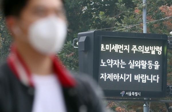 A masked man stands in front of a screen displaying an ultrafine dust emergency warning. (Yonhap)