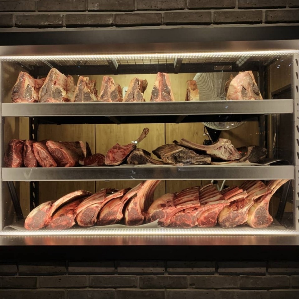 During dry aging, beef is left naked in a controlled environment allowing natural enzymes to break down connective tissue for a softer steak. Moisture is also lost during the process leading to more concentrated beefiness (The Porterhouse Butcher and More)