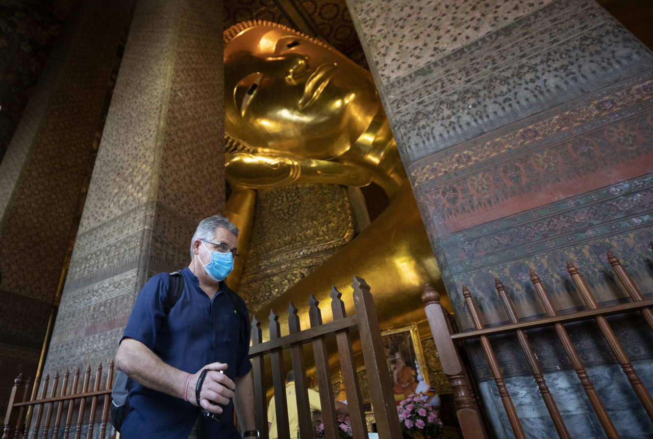 A tourist wearing protective mask walk in front of giant Buddha at Wat Pho temple in Bangkok, Thailand. (AP-Yonhap)