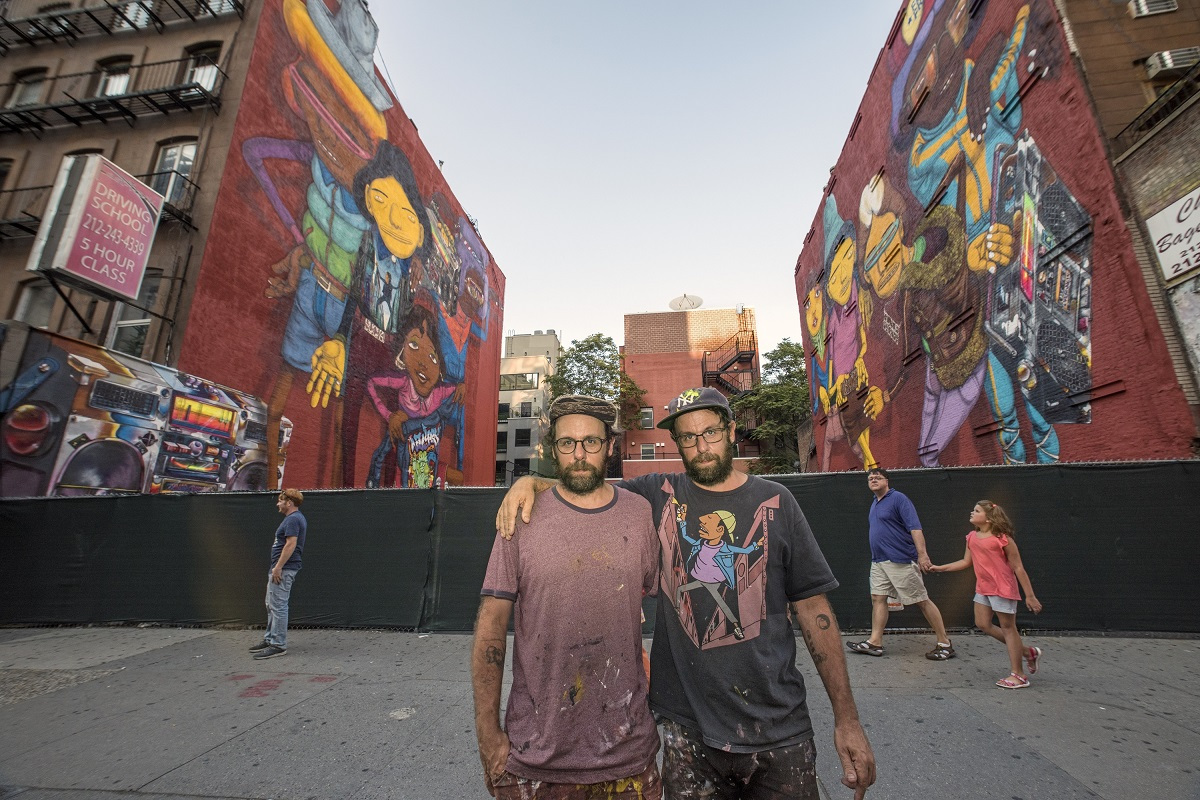 Osgemeos pose in front of their graffiti works. (Courtesy of artists and Lehmann Maupin)