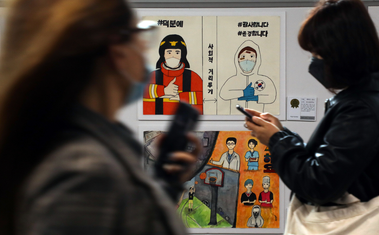 Citizens walk past posters on social distancing in a Seoul subway station on Tuesday. (Yonhap)